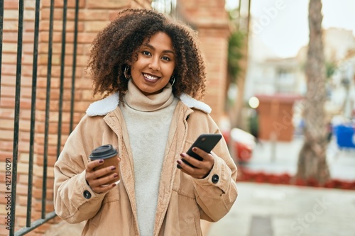 Young african american woman using smartphone and drinking coffee at the city. © Krakenimages.com