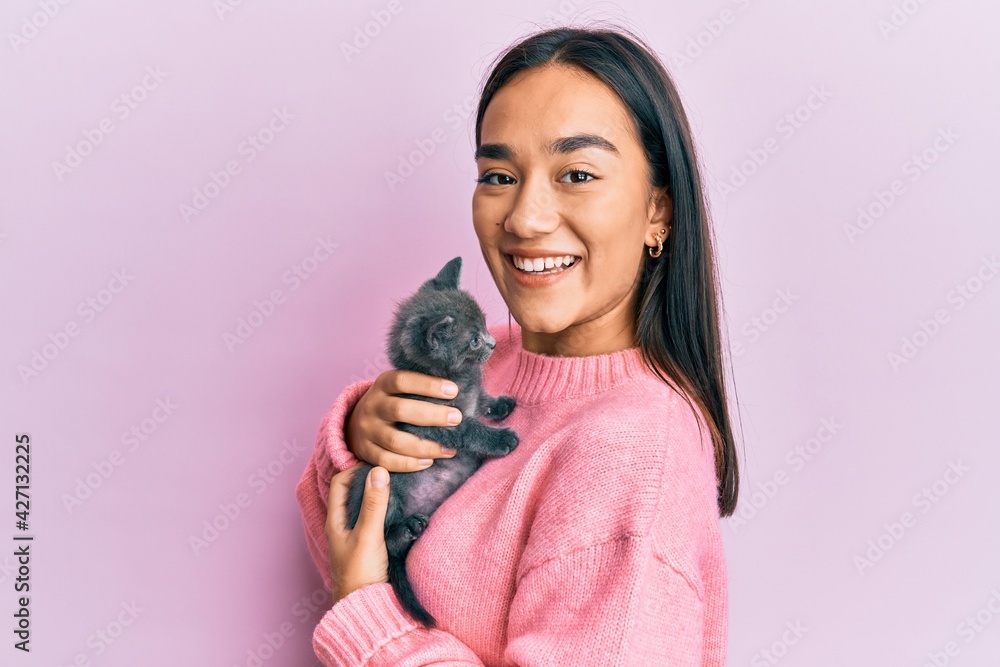 Young hispanic girl smiling happy holding cute cat over isolated pink background. Young hispanic girl smiling happy holding cute cat over isolated pink background.