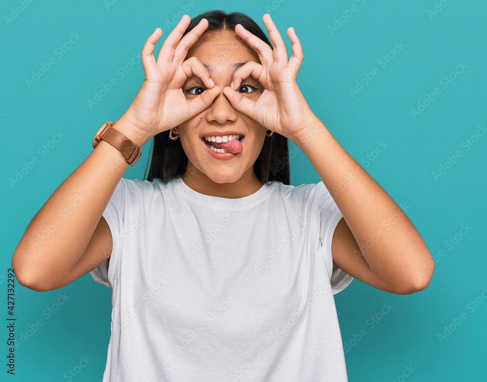 Young asian woman wearing casual white t shirt doing ok gesture like binoculars sticking tongue out, eyes looking through fingers. crazy expression. Young asian woman wearing casual white t shirt doing ok gesture like binoculars sticking tongue out, eyes looking through fingers. crazy expression.