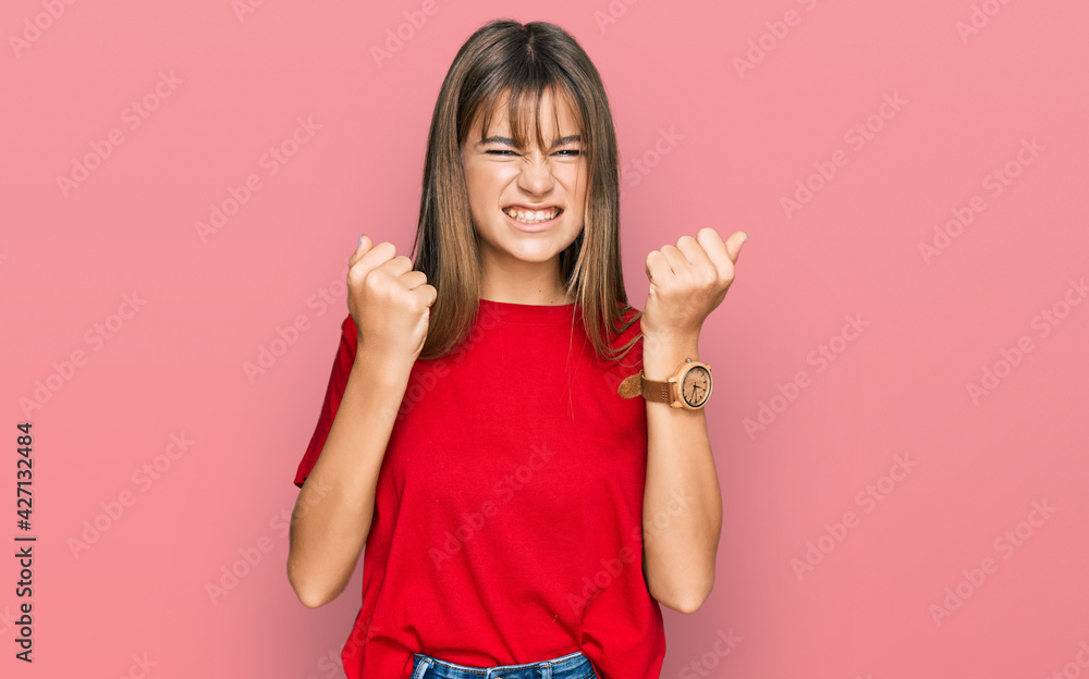 Teenager caucasian girl wearing casual red t shirt angry and mad raising fists frustrated and furious while shouting with anger. rage and aggressive concept. Teenager caucasian girl wearing casual red t shirt angry and mad raising fists frustrated and furious while shouting with anger. rage and aggressive concept.