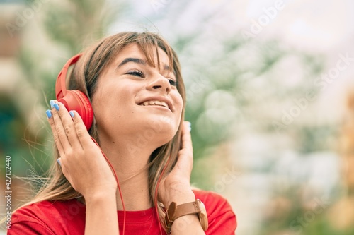 Caucasian teenager girl smiling happy using headphones at the city.