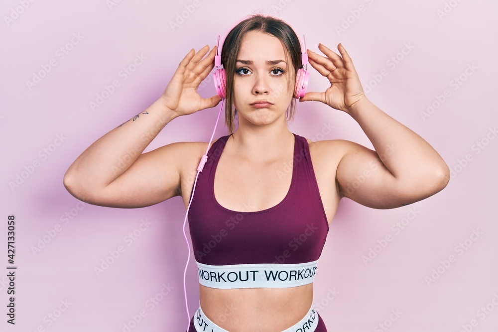 Young hispanic girl wearing gym clothes and using headphones depressed and worry for distress, crying angry and afraid. sad expression. Young hispanic girl wearing gym clothes and using headphones depressed and worry for distress, crying angry and afraid. sad expression.