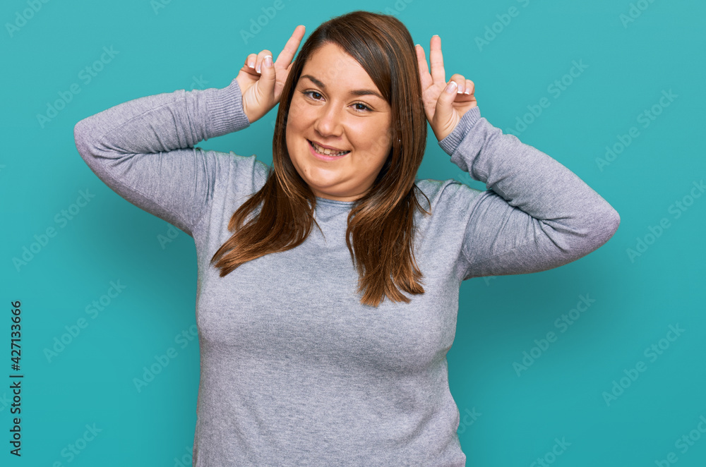 Beautiful brunette plus size woman wearing casual clothes posing funny and crazy with fingers on head as bunny ears, smiling cheerful Beautiful brunette plus size woman wearing casual clothes posing funny and crazy with fingers on head as bunny ears, smiling cheerful