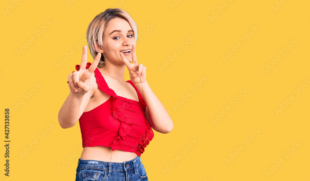 Young beautiful blonde woman wearing casual clothes smiling looking to the camera showing fingers doing victory sign. number two. Young beautiful blonde woman wearing casual clothes smiling looking to the camera showing fingers doing victory sign. number two.