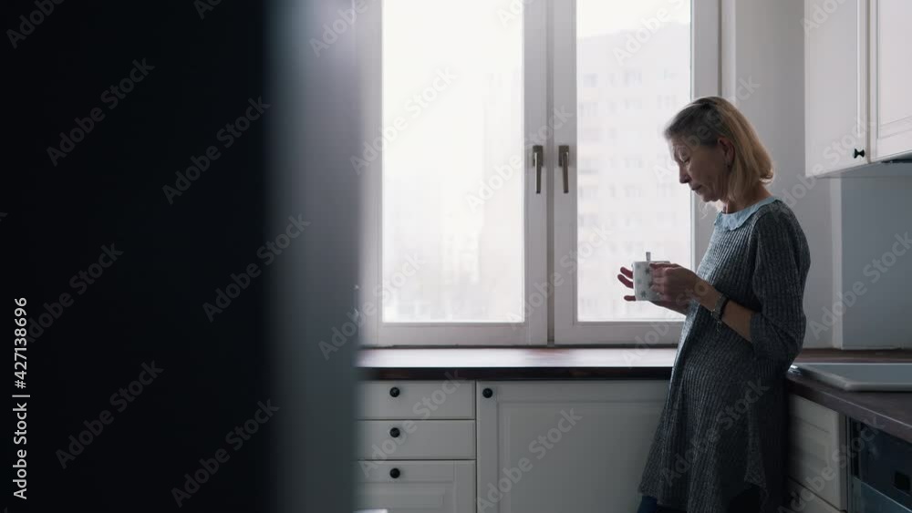 Lonely elderly woman drinking coffee standing at her kitchen. High quality 4k footage Lonely elderly woman drinking coffee standing at her kitchen. High quality 4k footage