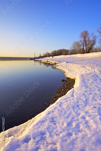 Morning on the bank of the Ob. Melting spring snow on the curve of the river bank, bare trees against the blue sky. Novosibirsk, Siberia, Russia © ArhSib