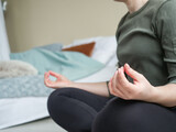 Woman sitting on floor in posture of meditation close up. Girl doing meditative practice in lotus position in bedroom. Active life in self-isolation.