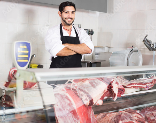 Portrait of cheerful man butcher who is posing with meat in the market.