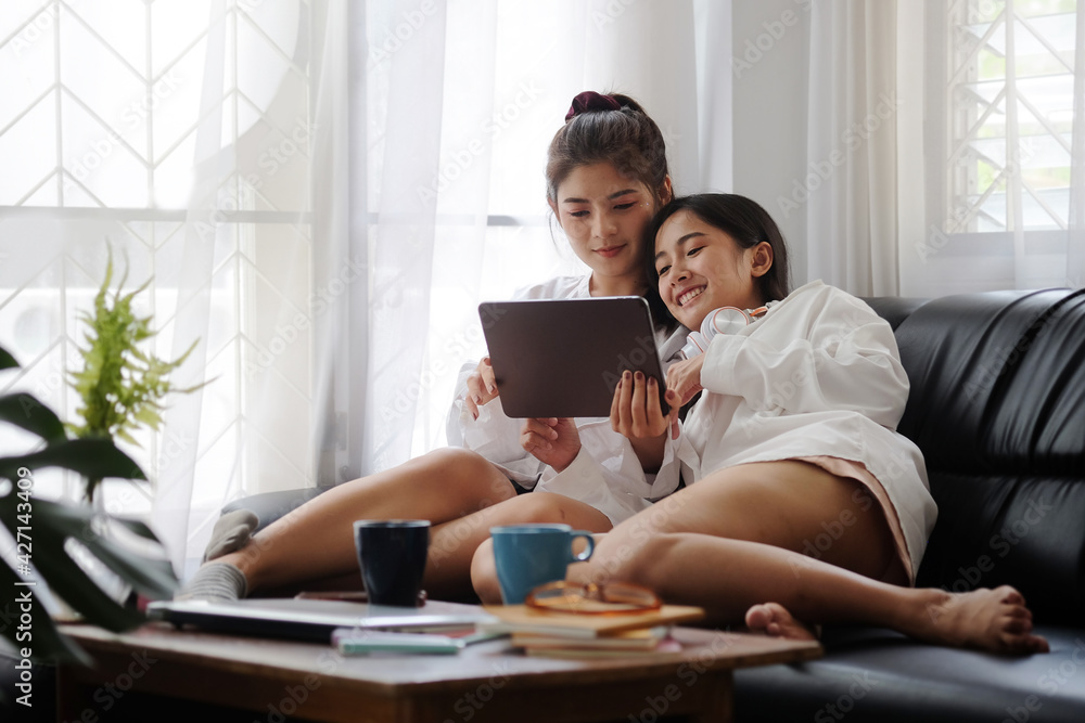 Cropped shot view beautiful young asian women LGBT lesbian happy couple sitting on sofa using laptop a computer and phone in living room at home. LGBT lesbian couple together. Cropped shot view beautiful young asian women LGBT lesbian happy couple sitting on sofa using laptop a computer and phone in living room at home. LGBT lesbian couple together.
