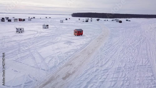 Flying away from the village of ice fishing huts with a drone over the frozen lake with a partly cloudy sky