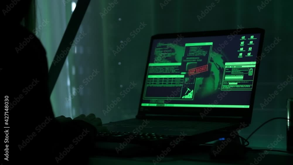 a criminal hackergirl with black hood using laptop and big computers to hack network system from her dark hacker neon room. a criminal hackergirl with black hood using laptop and big computers to hack network system from her dark hacker neon room.