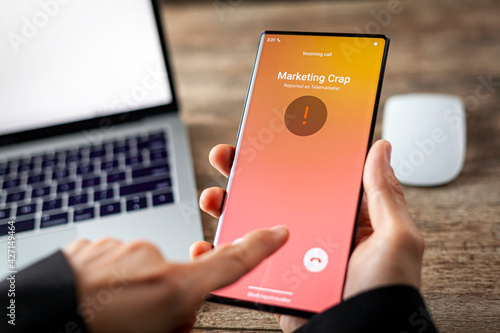 Concept image showing an office setting where a professional is receiving an unwanted robocall on her phone. The network provider detect the scam and put marketing crap notice. woman rejects the call. photo