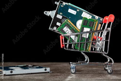 A concept image with a small shopping cart filled with computer parts including RAM memory cards and a hard drive. Shopping for technology, consumer electronics, upgrading computer themes.