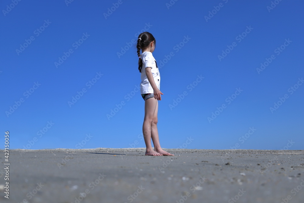 快晴の空と砂場に立つ少女