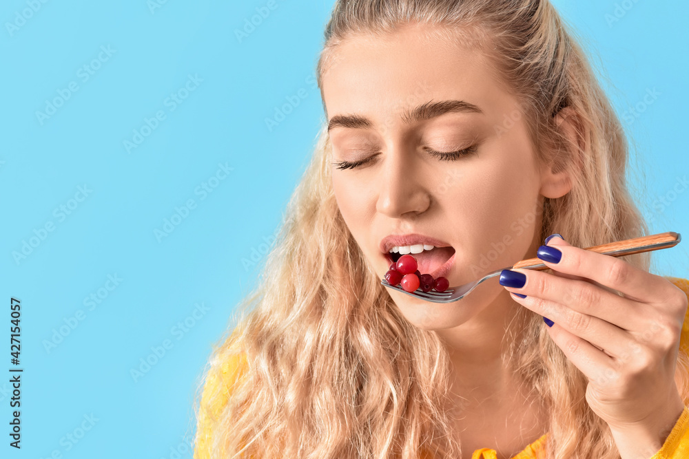 Beautiful young woman eating cranberry on color background, closeup Beautiful young woman eating cranberry on color background, closeup