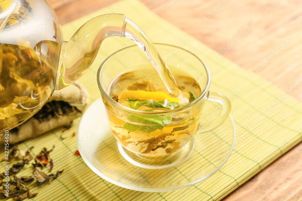 Pouring of green tea from teapot into cup on wooden background Pouring of green tea from teapot into cup on wooden background