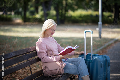  Young tourist woman sitting in the park with book.