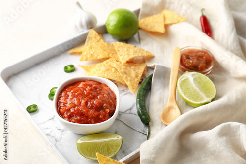 Tray with bowl of tasty salsa sauce and nachos on light background