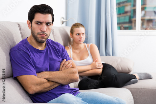 Young man sitting on sofa at home offended after quarrel with wife