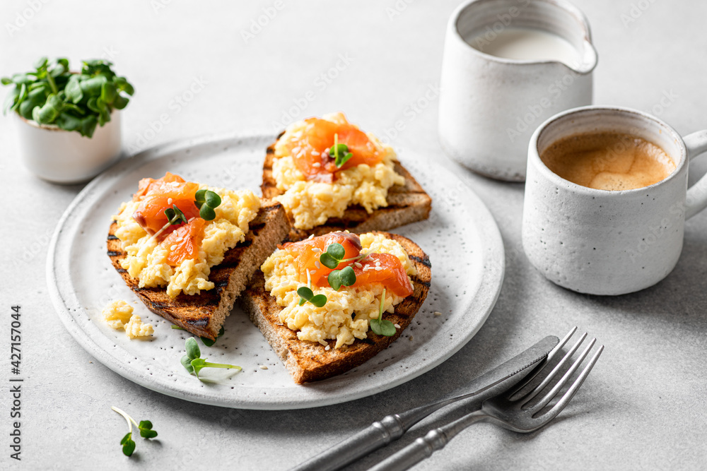 Scrambled egg sandwich with salmon on a ceramic plate on a white background, delicious and healthy breakfast, selective focus