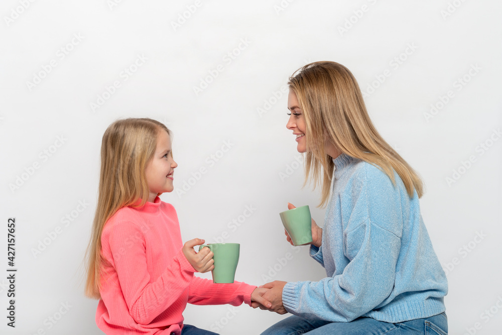 Young mother and daughter with cups of tea spends time together Young mother and daughter with cups of tea spends time together