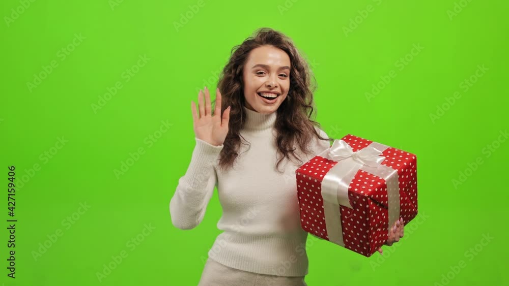The woman is standing and looking at the camera. She is holding the gift and waving. She is standing on a green background. Green screen. 4K The woman is standing and looking at the camera. She is holding the gift and waving. She is standing on a green background. Green screen. 4K
