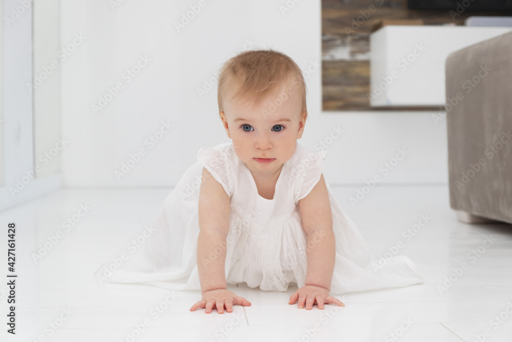 Cute little funny caucasian blonde baby girl in white dress, crawling on fours on floor at home Cute little funny caucasian blonde baby girl in white dress, crawling on fours on floor at home