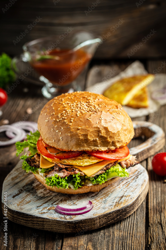 Homemade burger with grilled beef meat, vegetables, sauce on rustic wooden background. fast food and junk food concept