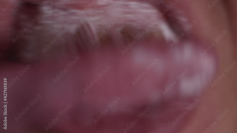 Extreme close-up view of person brushing teeth with pink toothbrush and tooth-powder. Morning hygiene. Macro view of open mouth and lips. Extreme close-up view of person brushing teeth with pink toothbrush and tooth-powder. Morning hygiene. Macro view of open mouth and lips.