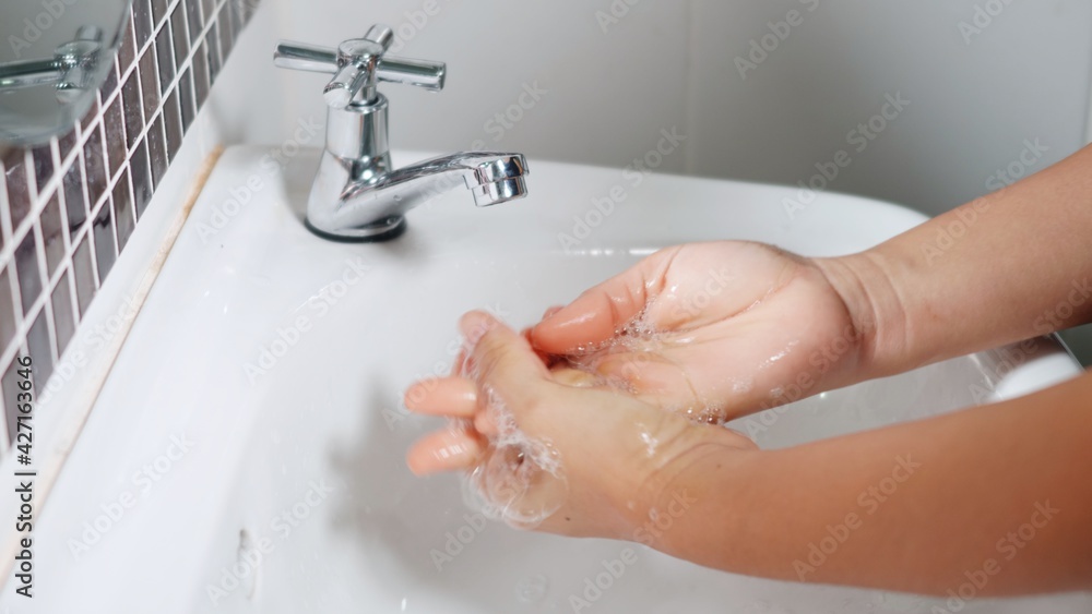 Closeup young woman hands using soap and washing hands under the water tap, female wash their palms with white bubbles in the sink at hotel bathroom to hygiene protect her from Covid-19 Closeup young woman hands using soap and washing hands under the water tap, female wash their palms with white bubbles in the sink at hotel bathroom to hygiene protect her from Covid-19