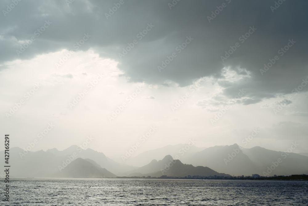 Summer landscape with views of the Mediterranean coast. Layers of mountains on the horizon, rays of the sun breaking through the clouds. Evening time before sunset. Antalya, Turkey
