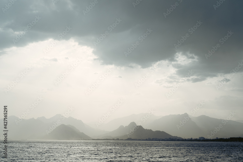 Summer landscape with views of the Mediterranean coast. Layers of mountains on the horizon, rays of the sun breaking through the clouds. Evening time before sunset. Antalya, Turkey Summer landscape with views of the Mediterranean coast. Layers of mountains on the horizon, rays of the sun breaking through the clouds. Evening time before sunset. Antalya, Turkey