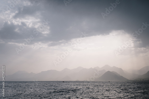 Summer landscape with views of the Mediterranean coast. Layers of mountains on the horizon, rays of the sun breaking through the clouds. Evening time before sunset. Antalya, Turkey © Alexey Oblov