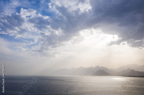 Summer landscape with views of the Mediterranean coast. Layers of mountains on the horizon, rays of the sun breaking through the clouds. Evening time before sunset. Antalya, Turkey