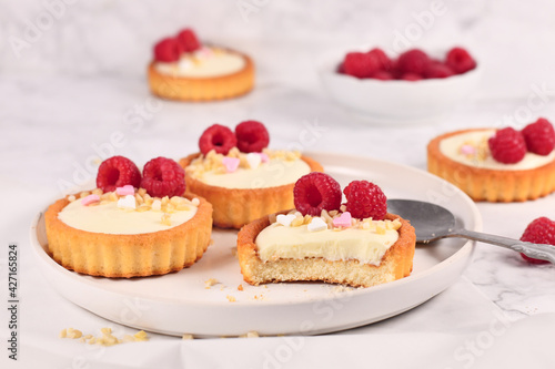 Small tartlet pastries with white cream, topped with raspberry fruits and almond sprinkles