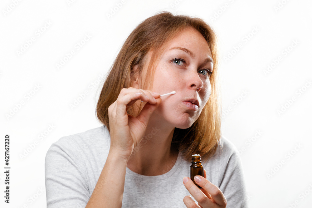 Portrait of a young woman smearing medicine on a pimple on her face. White background. Acne and pimples Portrait of a young woman smearing medicine on a pimple on her face. White background. Acne and pimples
