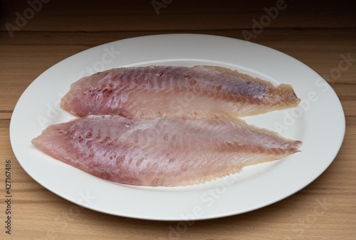 Two fillets of freshly caught redfish on a white plate, wooden table as a background