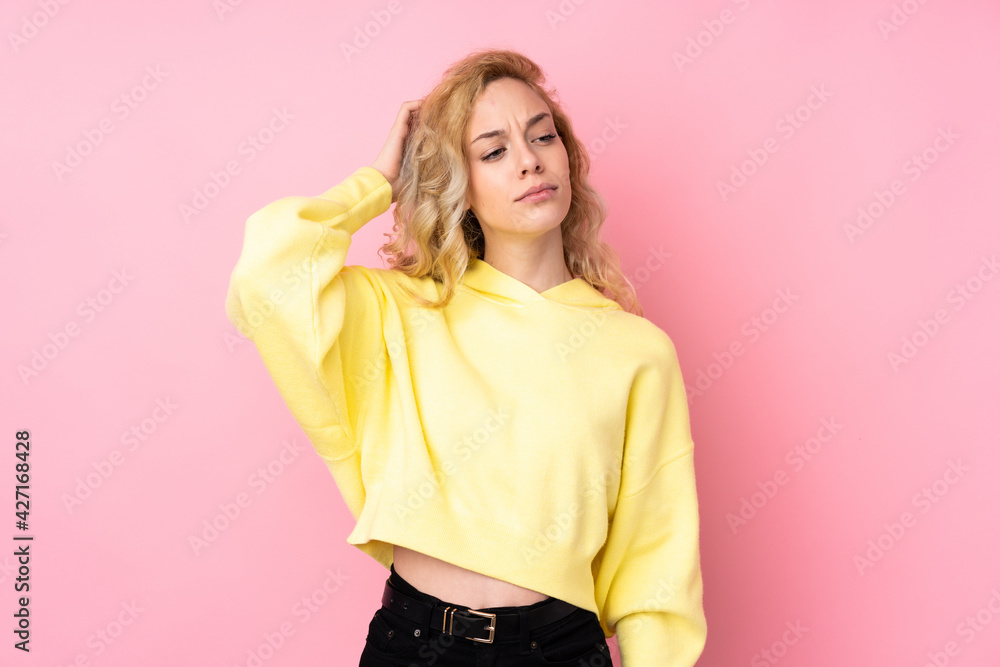 Young blonde woman wearing a sweatshirt isolated on pink background having doubts while scratching head Young blonde woman wearing a sweatshirt isolated on pink background having doubts while scratching head