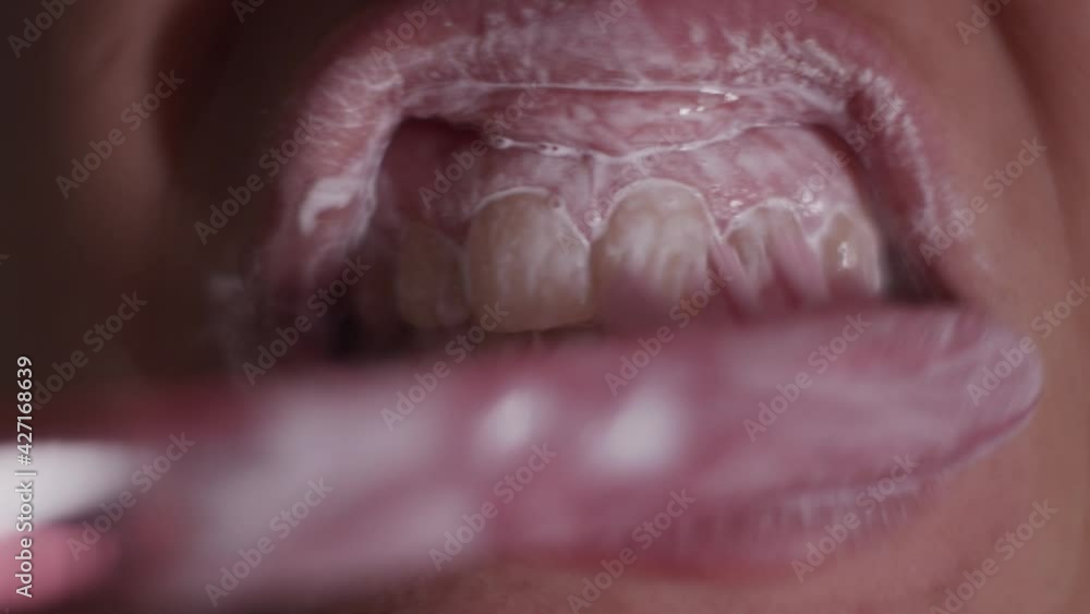 Extreme closeup view of person brushing teeth with pink toothbrush and