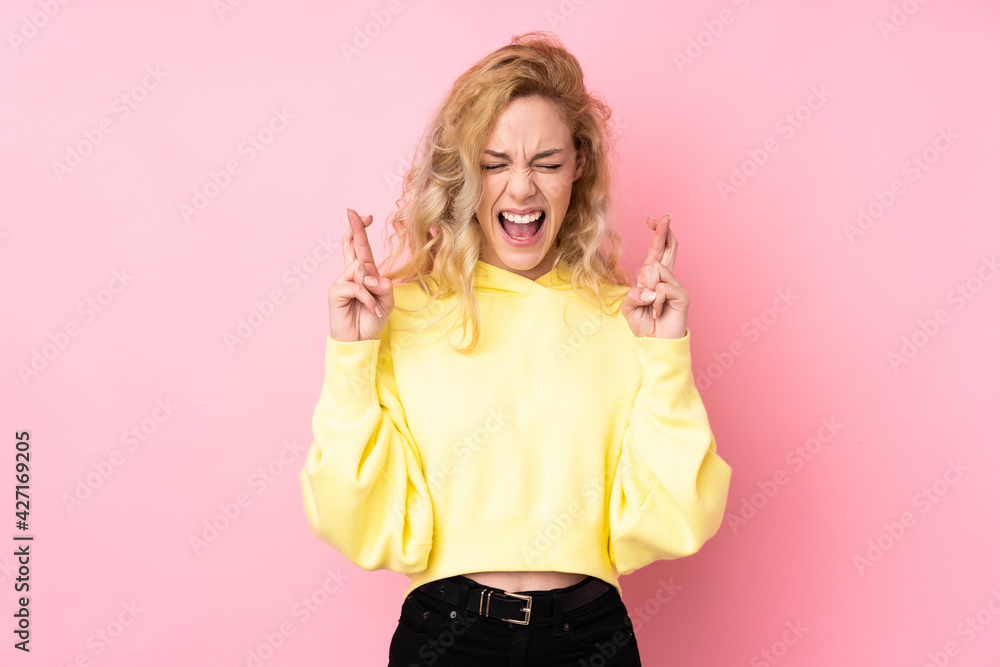 Young blonde woman wearing a sweatshirt isolated on pink background with fingers crossing Young blonde woman wearing a sweatshirt isolated on pink background with fingers crossing