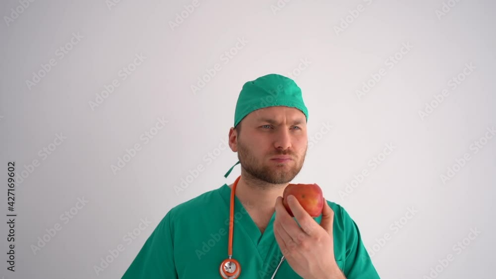 Young male bearded doctor therapist eating an apple during a break at work. Healthy eating, medical profession Young male bearded doctor therapist eating an apple during a break at work. Healthy eating, medical profession