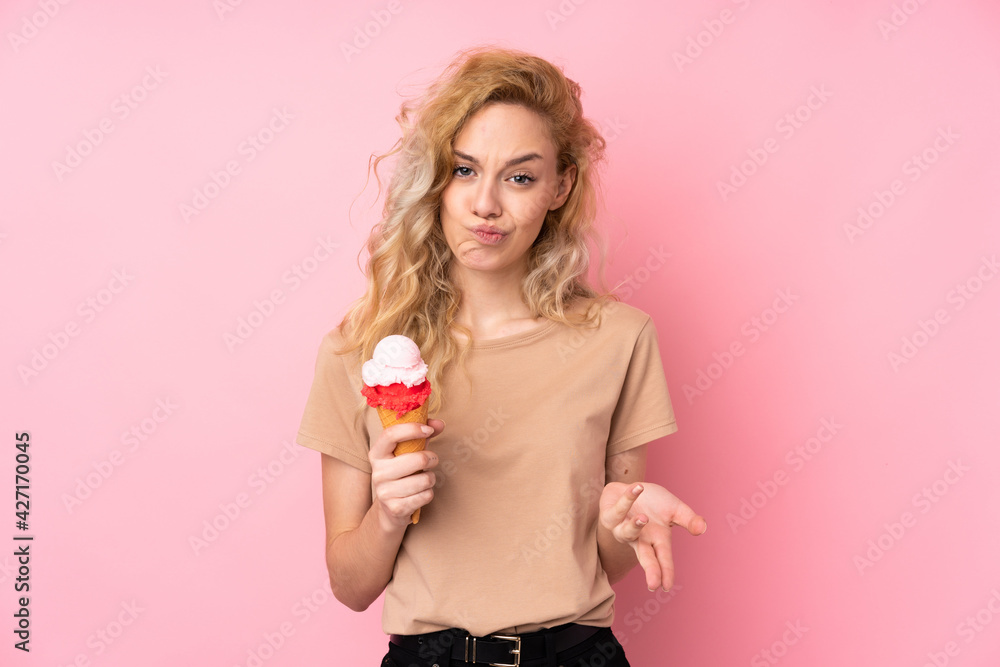 Young blonde woman holding a cornet ice cream isolated on pink background making doubts gesture while lifting the shoulders Young blonde woman holding a cornet ice cream isolated on pink background making doubts gesture while lifting the shoulders