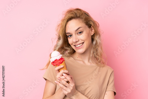 Young blonde woman holding a cornet ice cream isolated on pink background