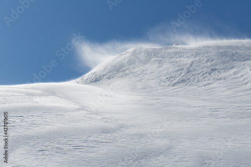 winter storm with wind blowing over snow cornice in snowy landscape