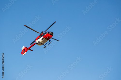 Red and white fire fighter helicopter flying in the air on background of blue clear sky. High quality photo. Transportation and technology concept