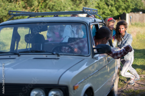 Young cheerful girls are pushing an old car. Women in the style of the 90s. © Светлана Лазаренко