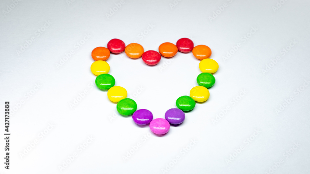 Selective focus of colorful button chocolates arranged in the shape of a heart on a white paper background. Selective focus of colorful button chocolates arranged in the shape of a heart on a white paper background.