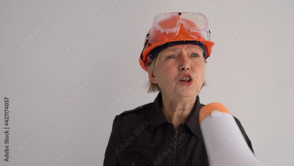 Mature woman construction engineer in an orange hard hat shouts into a megaphone. Important announcement, professional activity Mature woman construction engineer in an orange hard hat shouts into a megaphone. Important announcement, professional activity