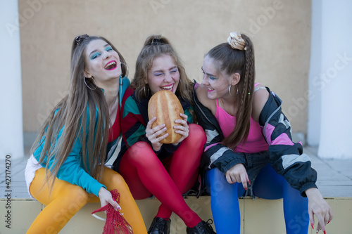 Beautiful country girls dressed in the style of the nineties are eating a roll and laughing. © Светлана Лазаренко