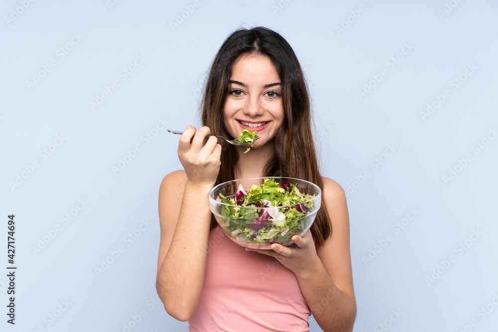 Young caucasian woman holding a salad isolated on blue background Young caucasian woman holding a salad isolated on blue background
